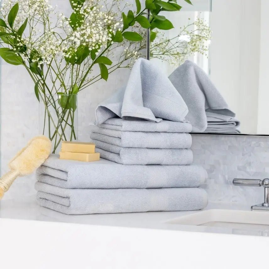 Stack of light blue Premium Turkish Cotton towels on a bathroom counter with a vase of flowers and soap.
