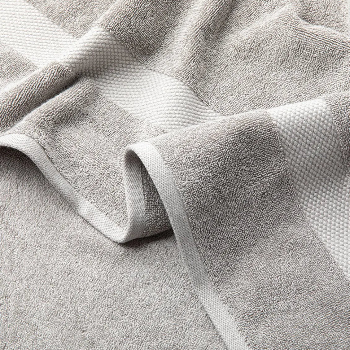 Close-up of a textured Premium Turkish Cotton gray towel with folds on a light gray background