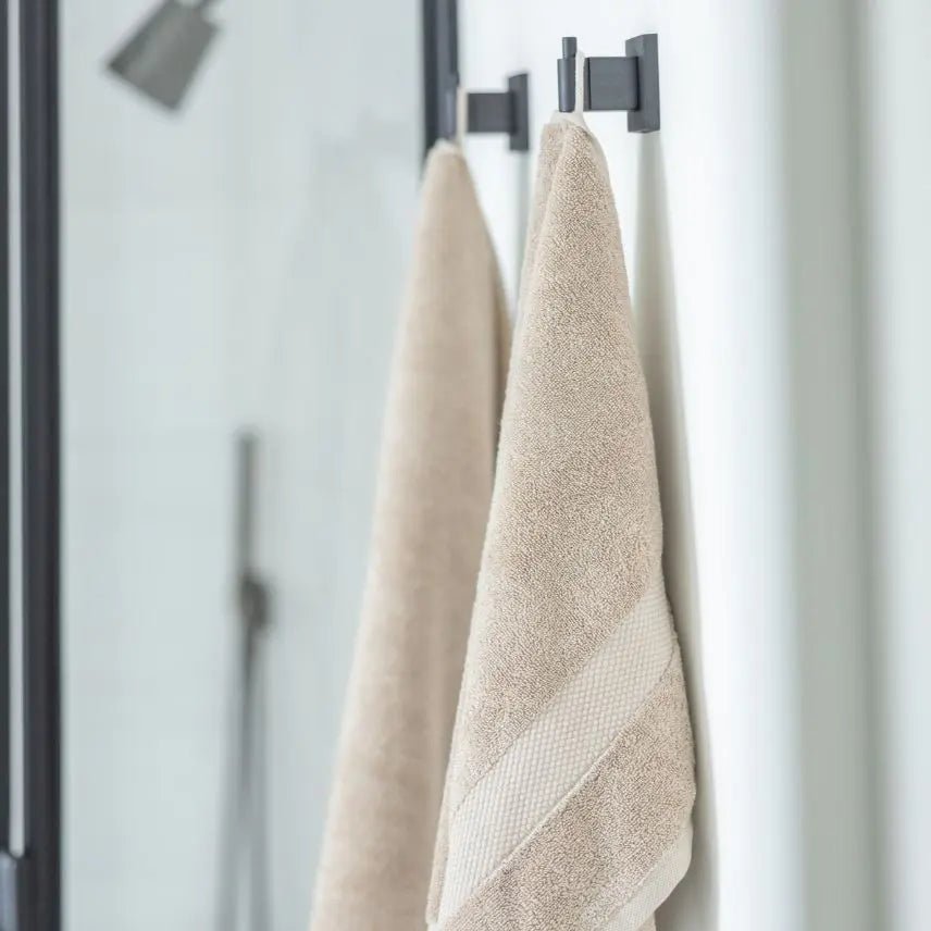 Two beige Turkish Cotton towels hanging on a black towel rack against a white wall.