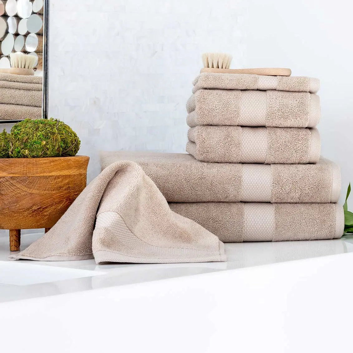 Stack of beige Premium Turkish Cotton towels on a white surface with a mirror and plant in the background