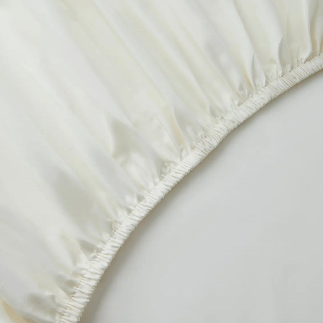 Close-up of an ivory white fitted sheet on a bed with a neutral background