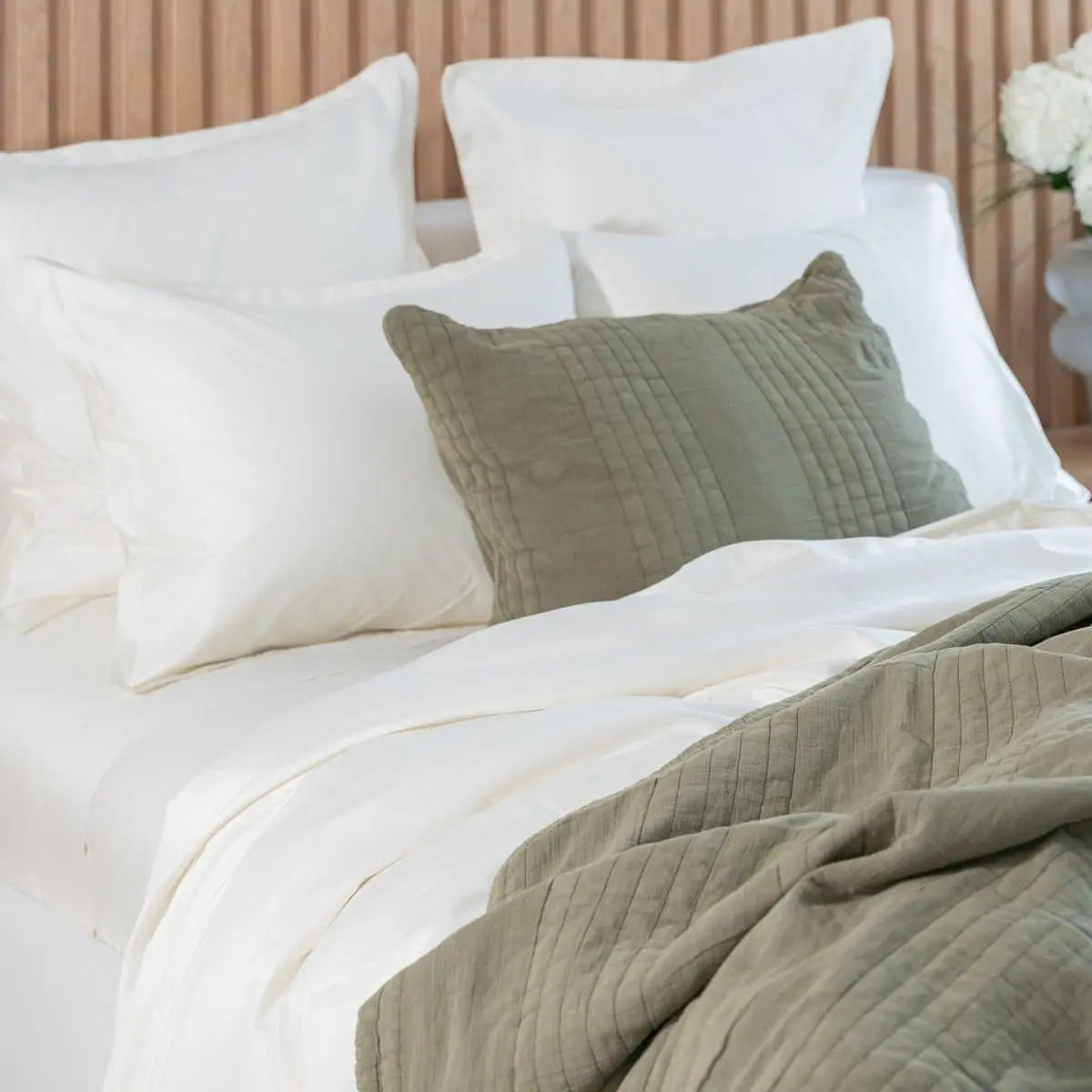 Bed with white and green bedding and pillows against a neutral wall.