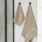 Two taupe beige towels hanging on hooks against a white bathroom wall.