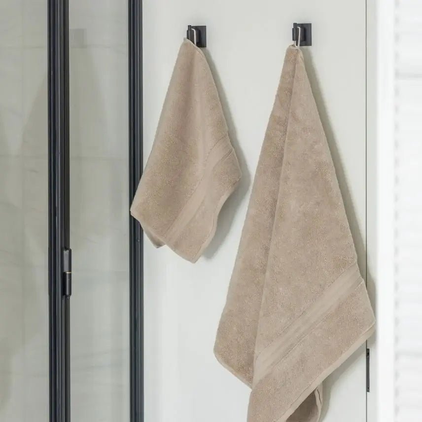 Two taupe beige towels hanging on hooks against a white bathroom wall.