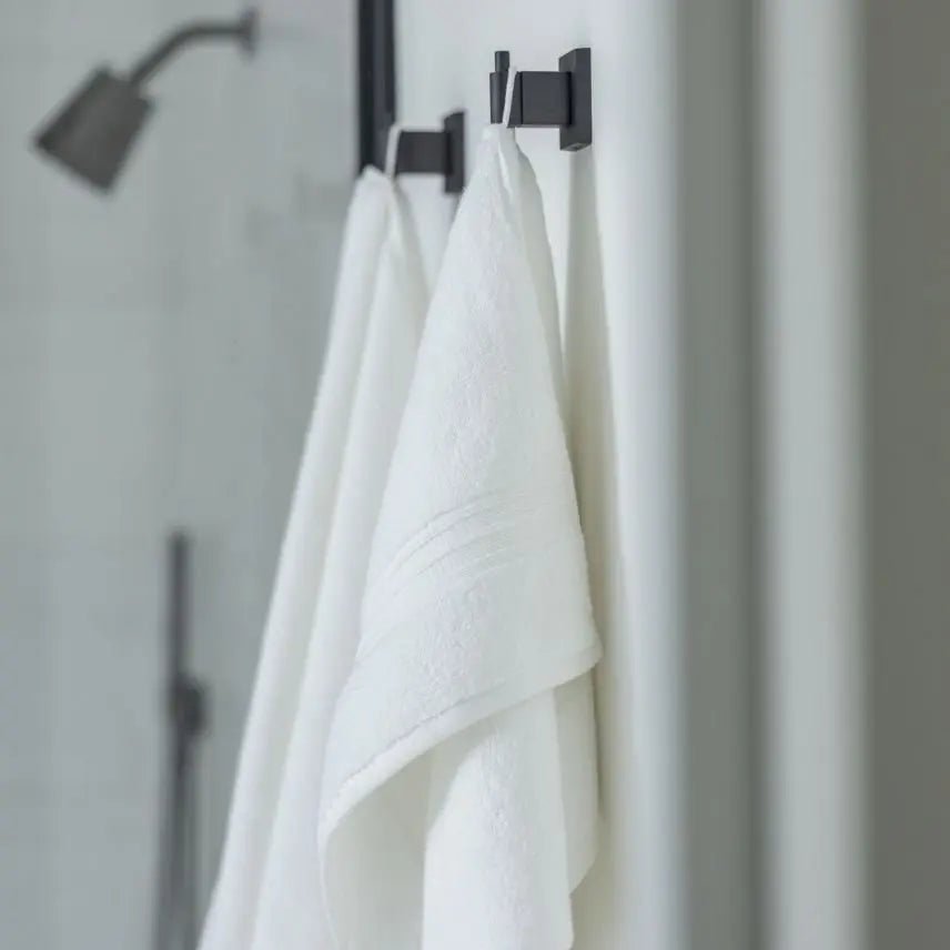 Two white super plush towels hanging from black hangers on a bathroom