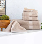 Stack of beige Premium Turkish Cotton towels on a white surface with a mirror and plant in the background