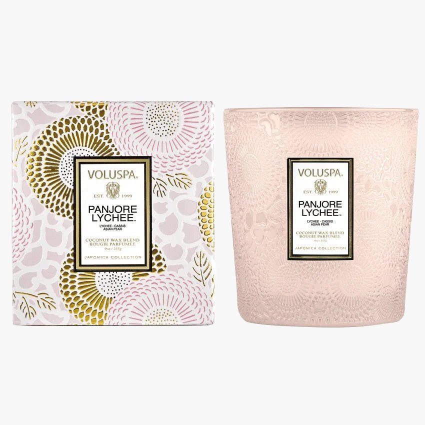 A Voluspa Panjore Lychee scented candle with a pink and white design on the packaging, featuring a floral pattern and a clear glass candle container.
