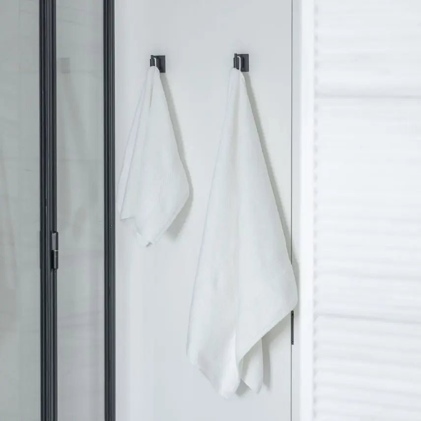 White Turkish cotton towels hanging on black hooks against a white wall.