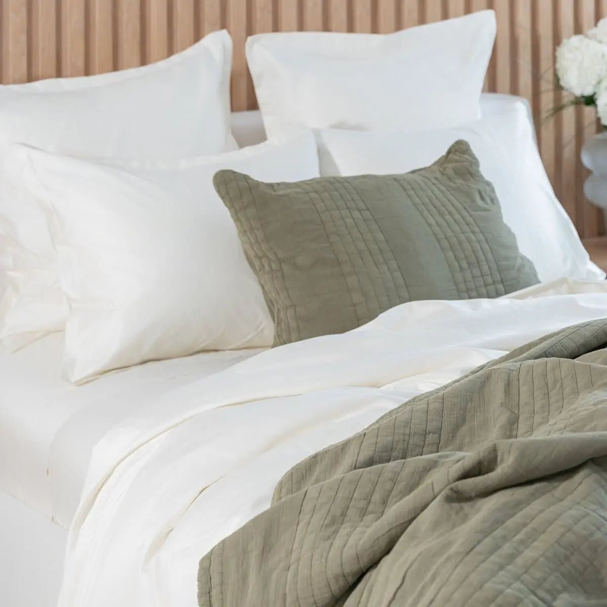 Bed with white and green bedding and pillows against a neutral wall.