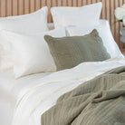 Bed with white and green bedding and pillows against a neutral wall.