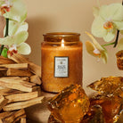 Voluspa Baltic Amber Large Jar Candle surrounded by amber rocks, flowers, and wood chips.