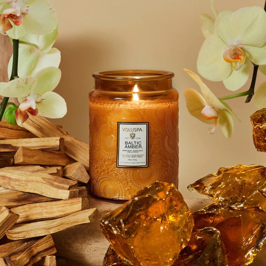 Voluspa Baltic Amber Large Jar Candle surrounded by amber rocks, flowers, and wood chips.